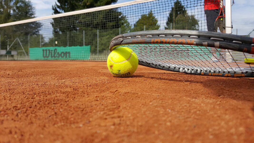 Raqueta y pelota apoyadas en el suelo de una pista de tenis