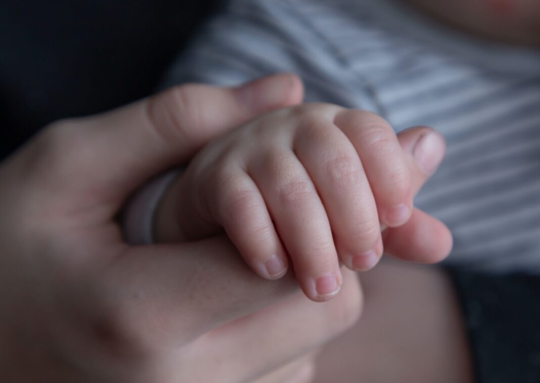 Padre o madre sujetando la mano de su hijo bebé